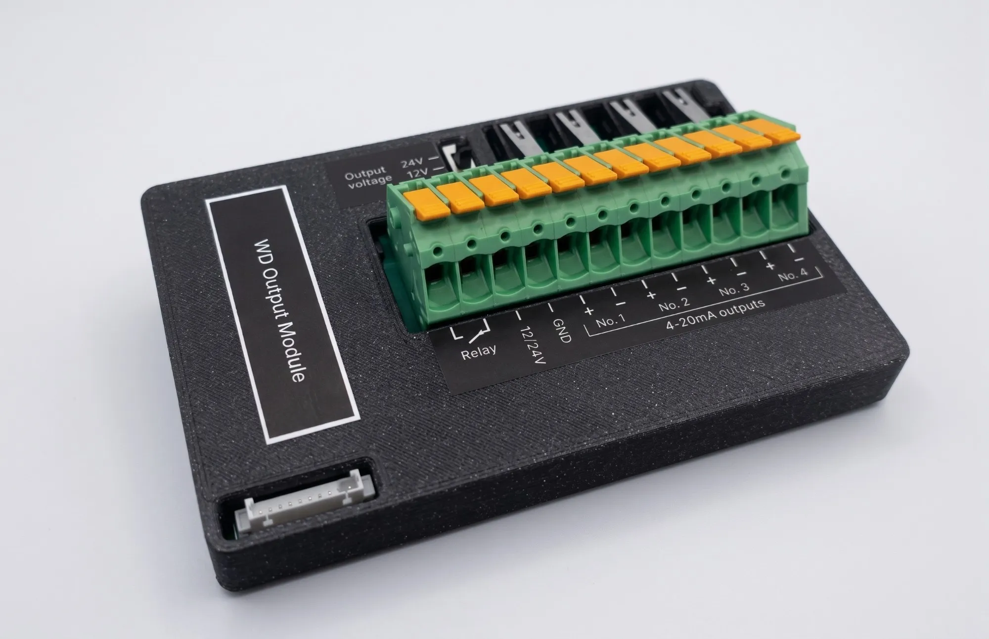 The WD Output Module: a black 3D-printed enclosure with a 12-pole green pluggable terminal block, an output voltage selector, wiring test buttons and a picoblade expansion connector